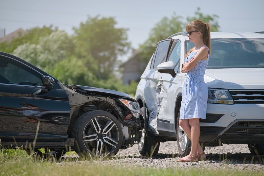 female driver looking stressed standing to the side of two vehicles crashed on road