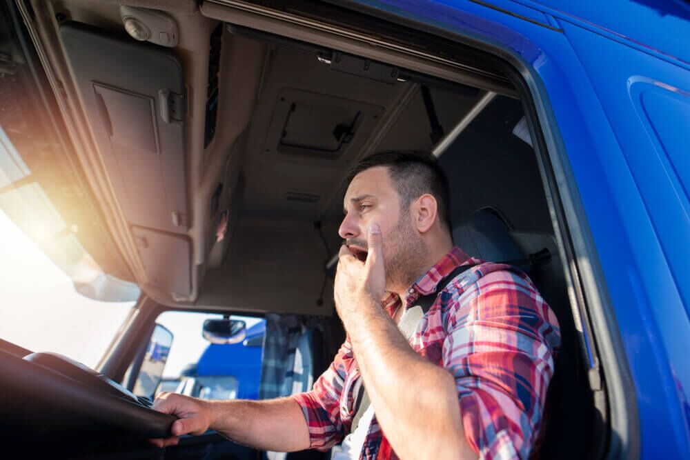 Truck driver yawning while driving. Trucker feeling sleepy and tired after long ride. Overworked people at job.