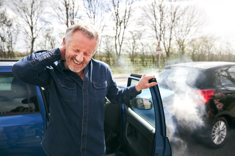 Senior male driver with whiplash injury getting out of car after traffic accident