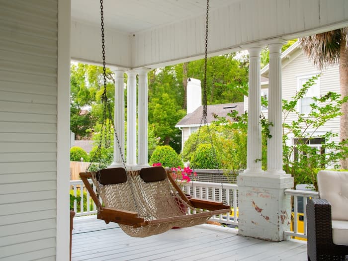 A cozy porch features a hanging swing chair made of woven material and supported by sturdy chains.