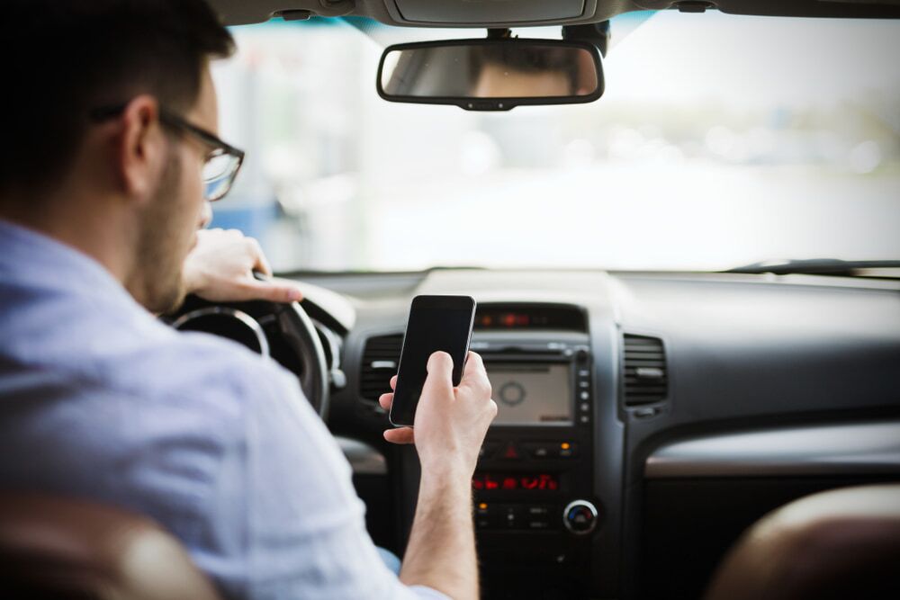 man driving a car while texting on phone