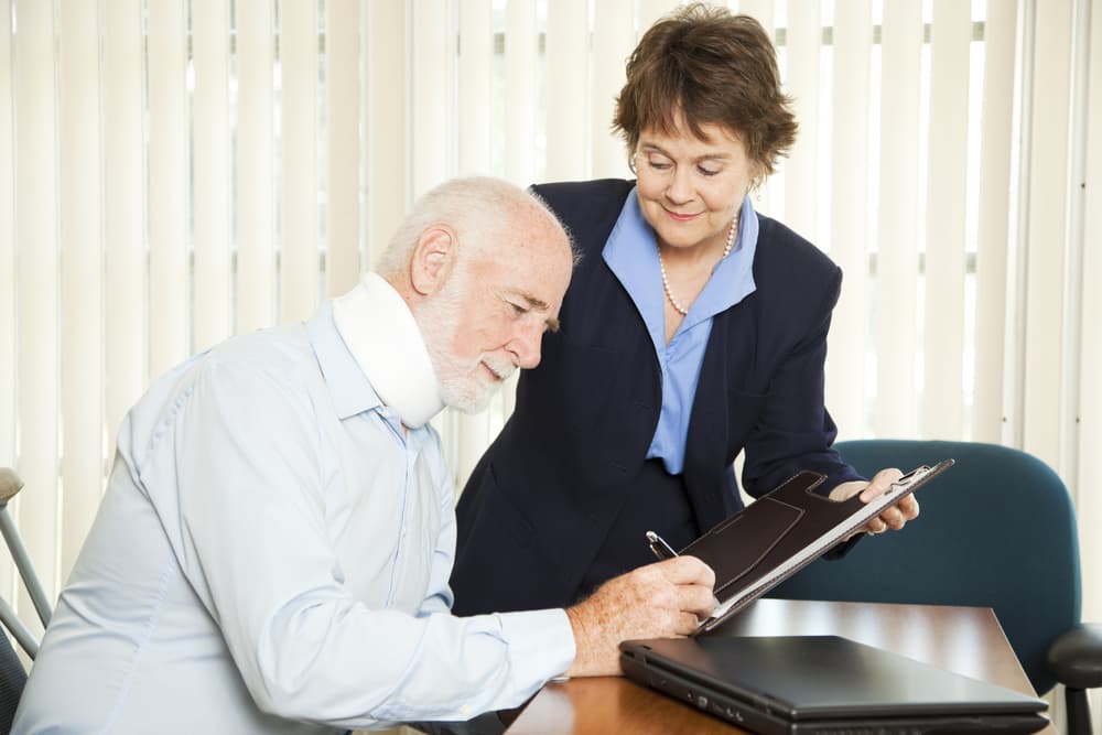 injured eldery man signing SSD paperwork with the help of a lawyer to endure maximum benefits