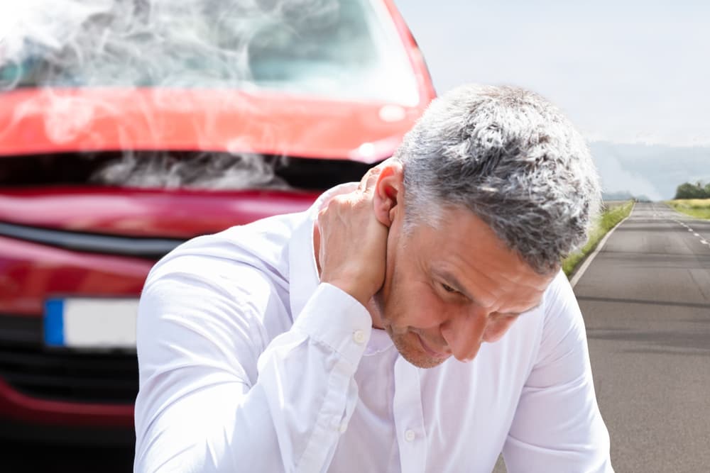 man holding back in pain with car wreck in the background