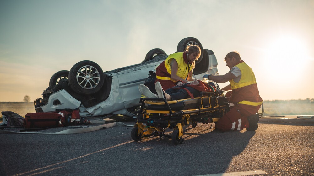 injured person being assisted on a stretcher in front of an accident scene