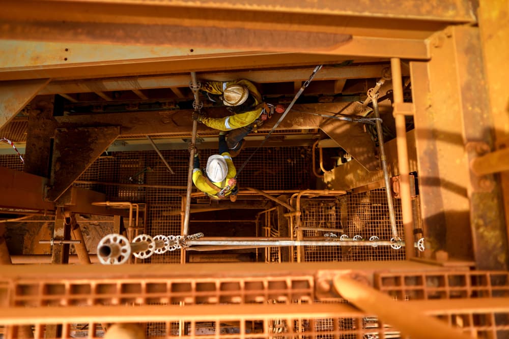 overhead view of two construction workers working on grated platform, no safety nets in place to catch dropped tools