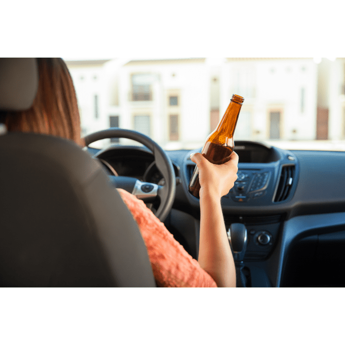 women holding alcoholic beverage behind the wheel of a car