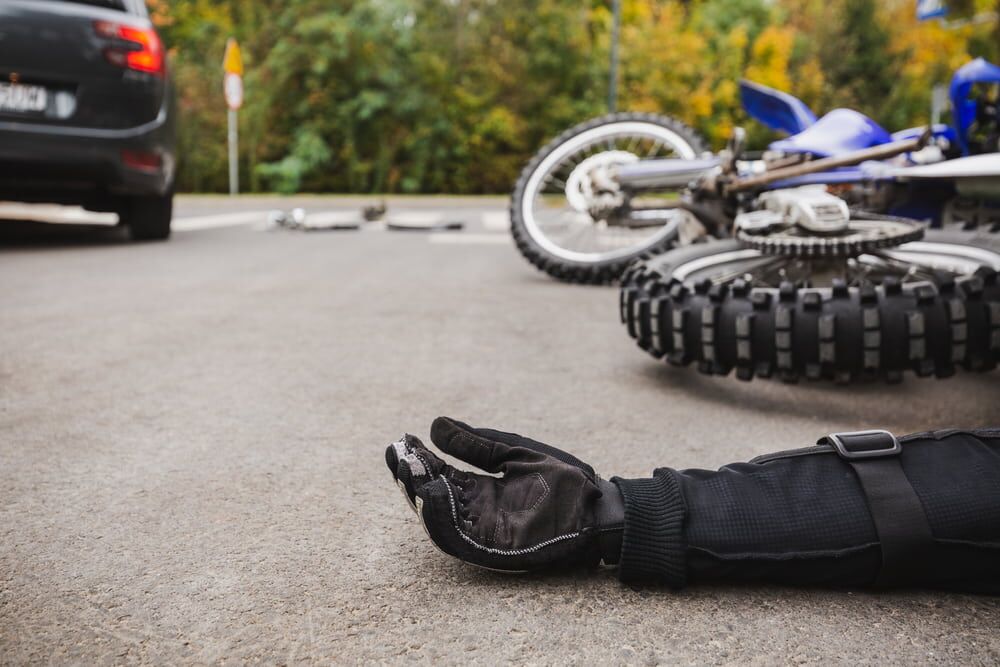 motorcycle accident depiction scene with crashed motorcycle lying on its side and close up of motorcyclists forearm on pavement