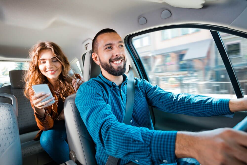 Smiling driver talking with female passenger. Woman holding mobile phone in hand.