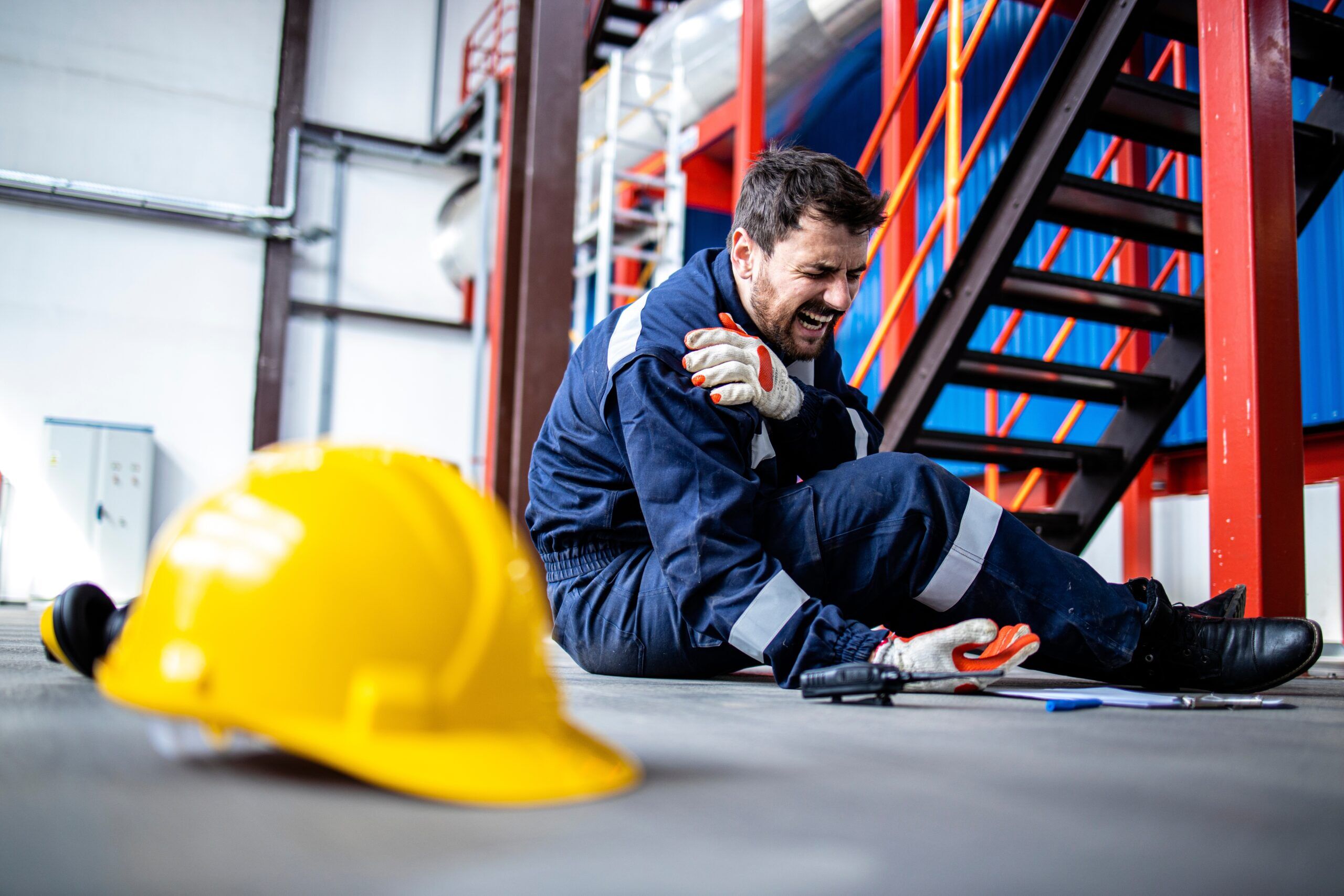 construction worker sitting on the ground holding his shoulder with a pained expression