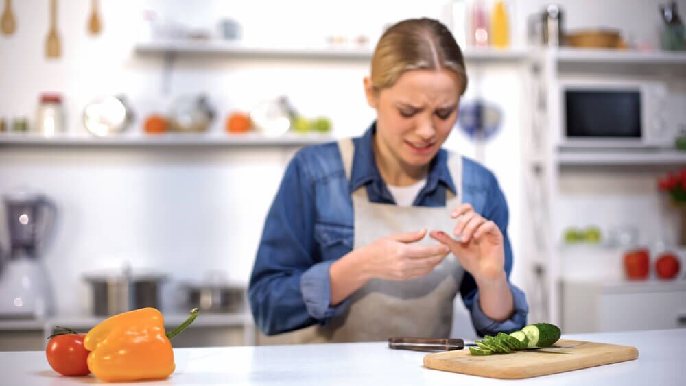 Female cut finger while slicing cucumber, accident in kitchen, household injury.