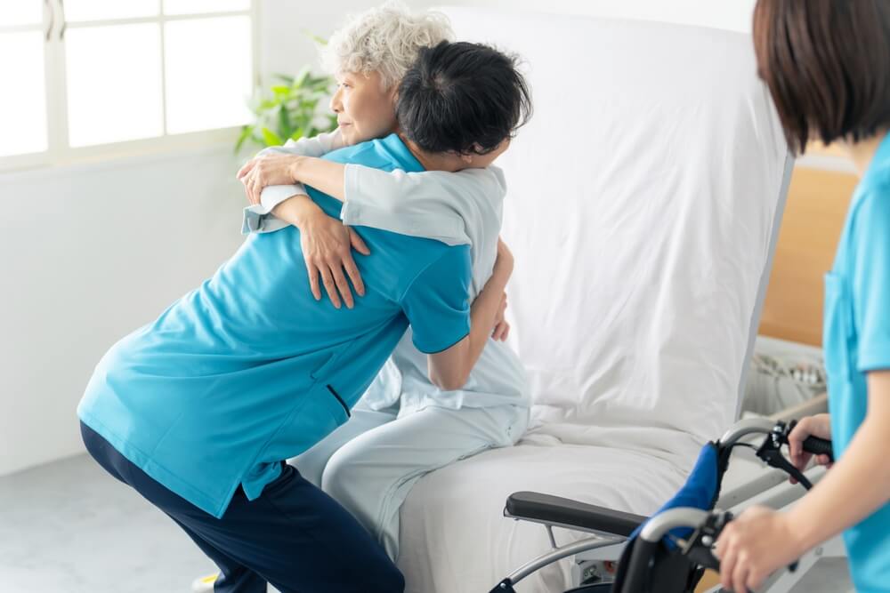 A caregiver transferring an elderly person from a nursing bed to a wheelchair.