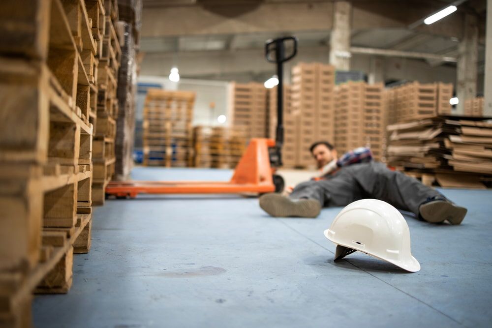 warehouse worker lying on the floor injured with white hard hat in foreground