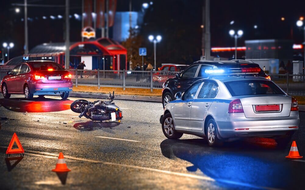 Motorcycle crash, night accident. Traffic police car with blue flashing lights investigate moto collision.